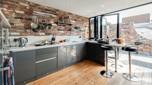 A modern kitchen with a brick wall, stainless steel appliances, and a bar area with stools. - Base Serviced Apartments - Sir Thomas Street (Liverpool)