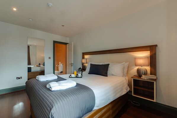 A hotel room with a bed, bedside table, lamp, and a mirror. - Base Serviced Apartments - Sir Thomas Street (Liverpool)