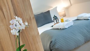 A neatly made bed with a grey quilt, a bedside lamp, and a small table with a bottle and glass. - Base Serviced Apartments - Sir Thomas Street (Liverpool)