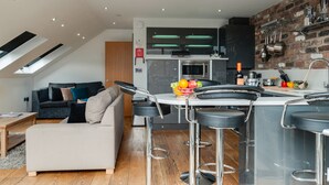 A modern kitchen with a built-in oven, bar stools, and a fruit bowl on the counter. - Base Serviced Apartments - Sir Thomas Street (Liverpool)