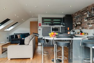 A modern kitchen with a built-in oven, bar stools, and a fruit bowl on the counter.