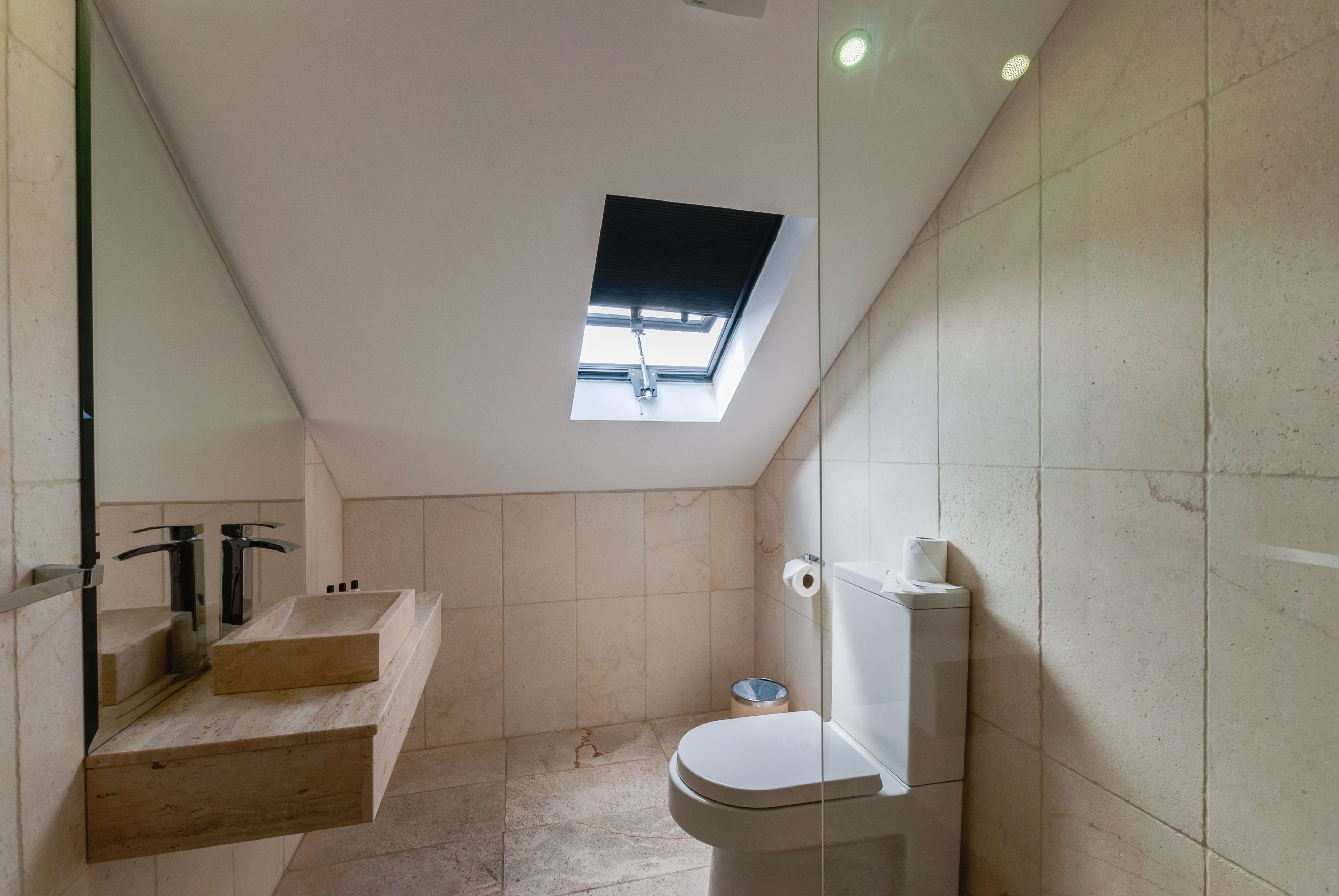 Et lille badeværelse med ovenlys, toilet og vaskebord med spejl.