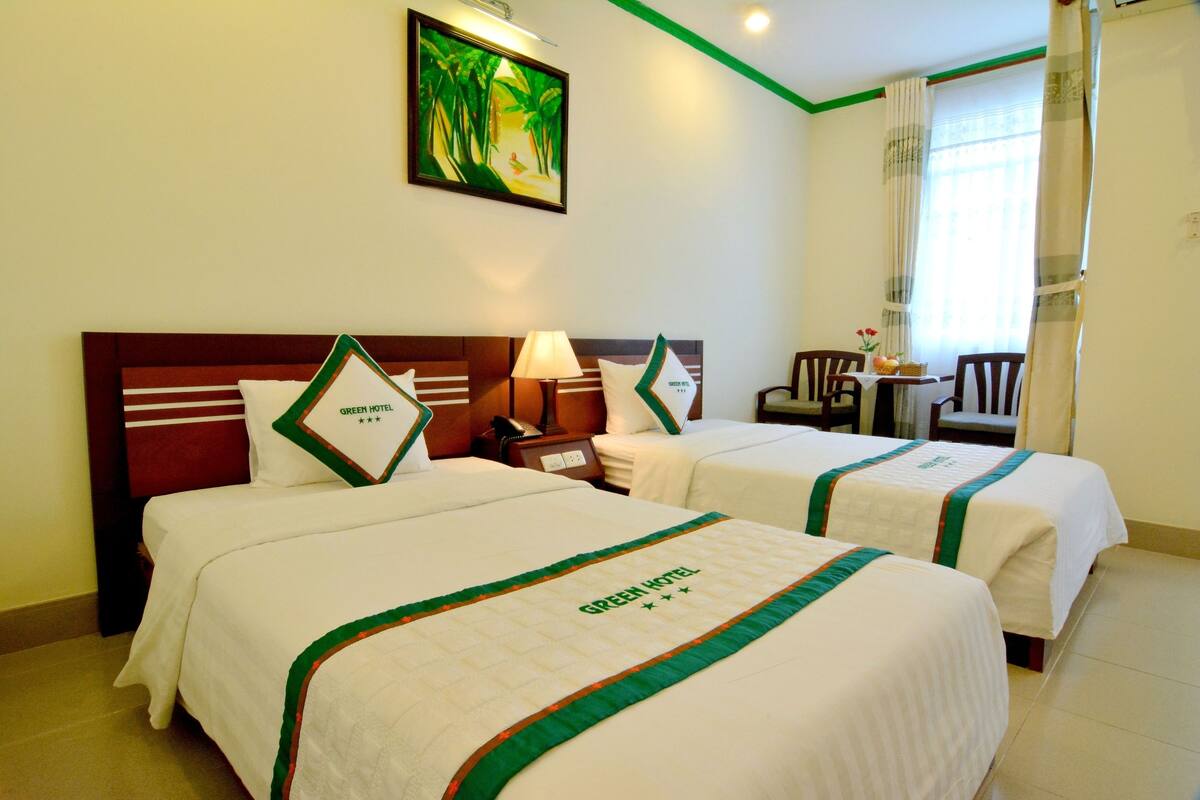A hotel room with two beds, a nightstand with a lamp, a painting on the wall, and a window with curtains.
