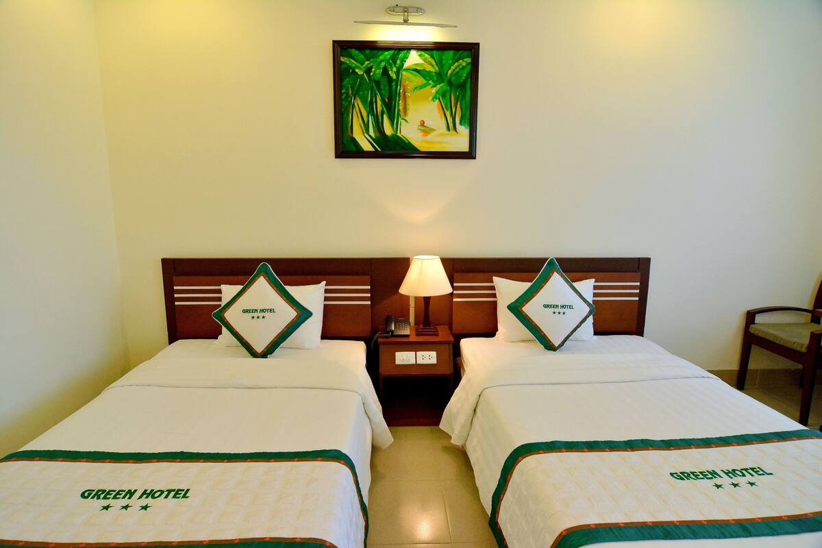 A hotel room with two beds, a nightstand with a lamp, a framed picture on the wall, and a chair.