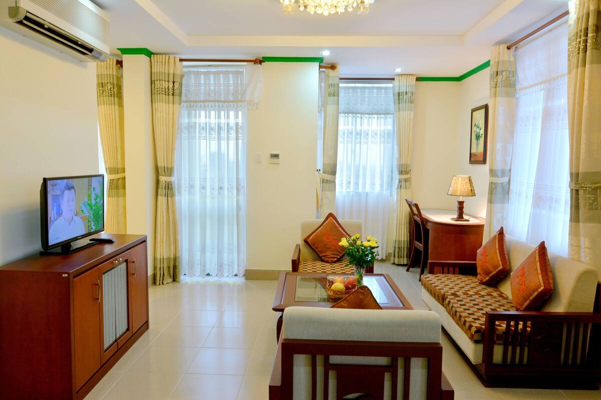 A living room with a sofa, a coffee table, a TV on a cabinet, and a dining area with a table and chairs.
