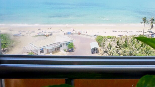 A beach view from a window overlooking a parking area with a building and palm trees. - Green Hotel (Ho Chi Minh City)