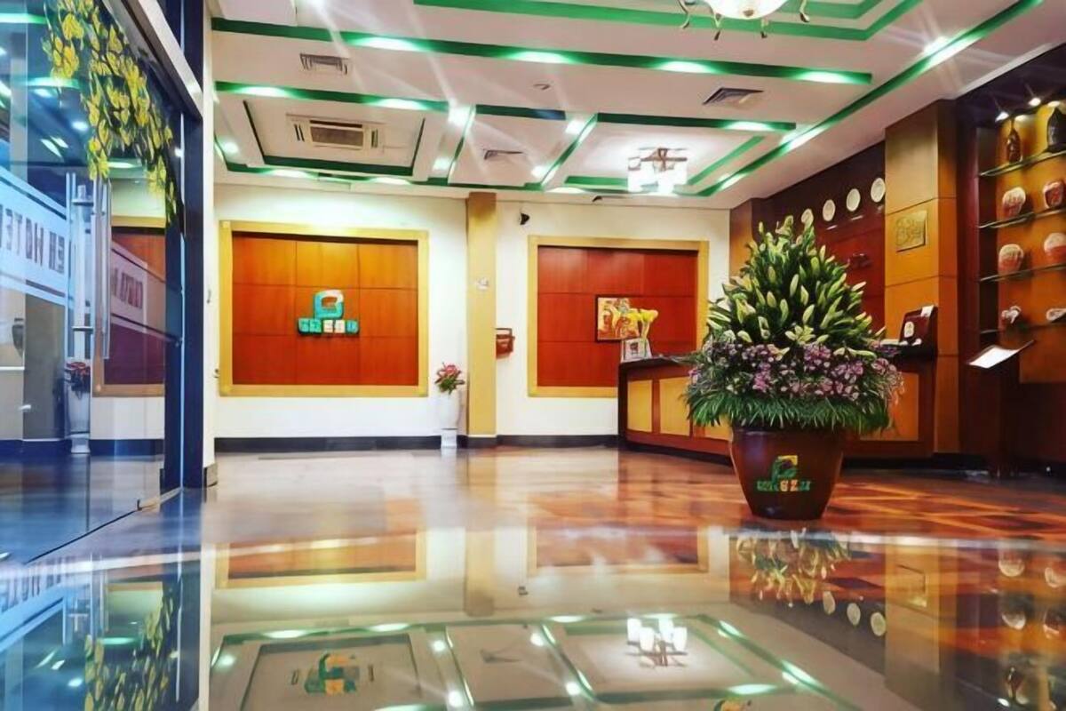 A hotel lobby with a reception desk, a large potted plant, and a wall with framed pictures.