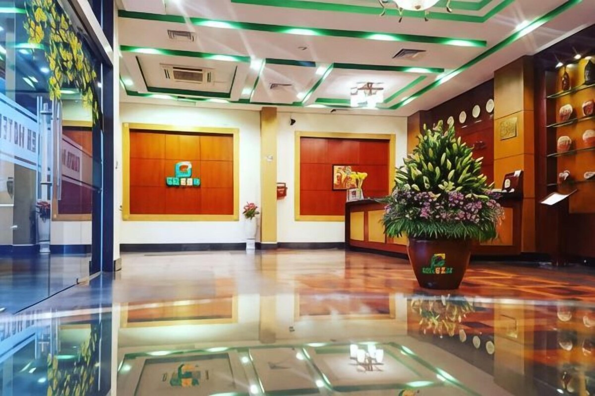 Una hall d'albergo con una reception, un'ampia pianta in vaso e una parete con quadri incorniciati.