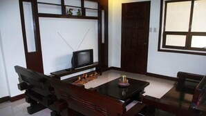 A living room with a television, a wooden bench, a table with a bottle, and a window. - Costa Villa Beach Resort (San Juan)
