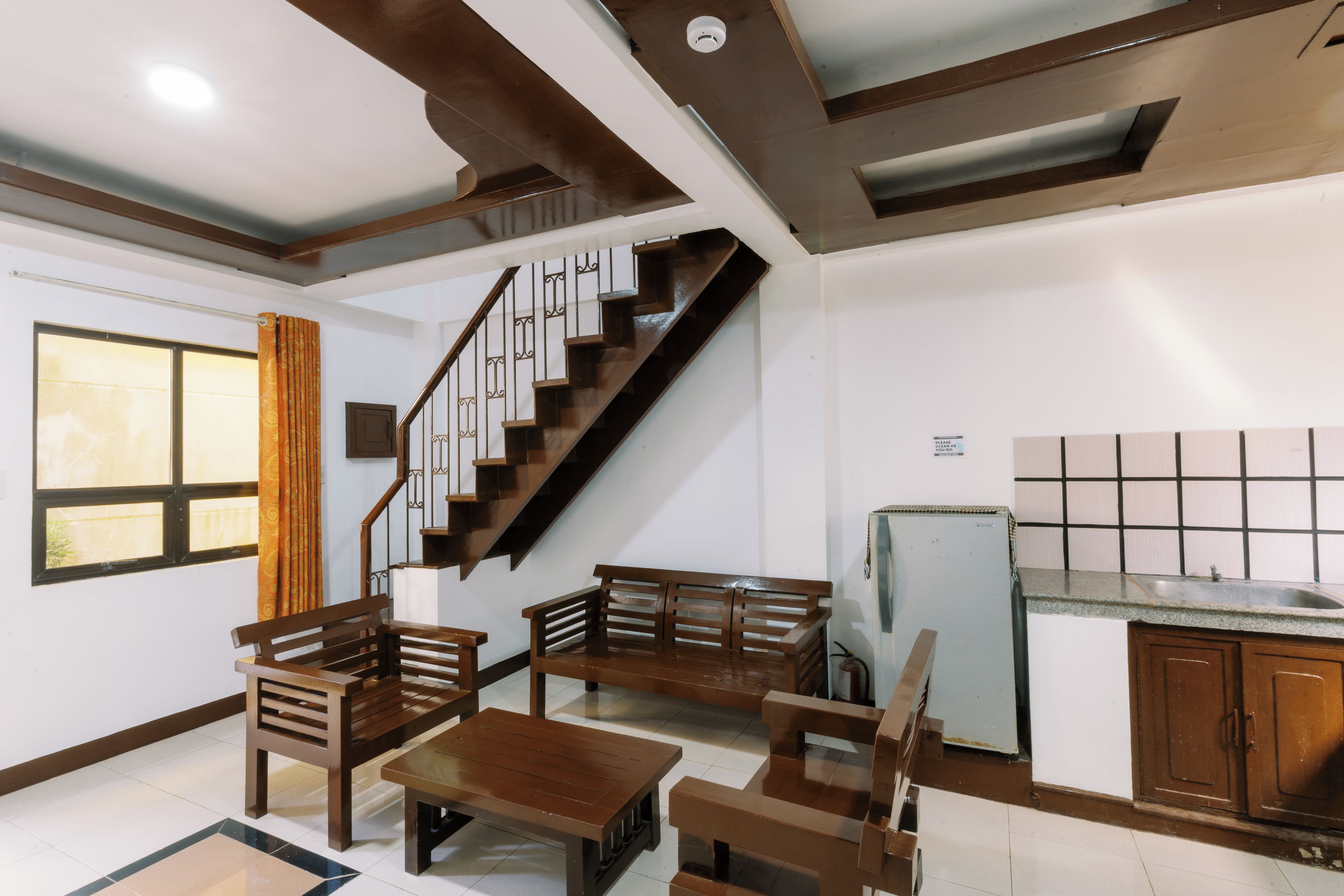A modern interior with a staircase, wooden furniture, a kitchen area, and a window with curtains.