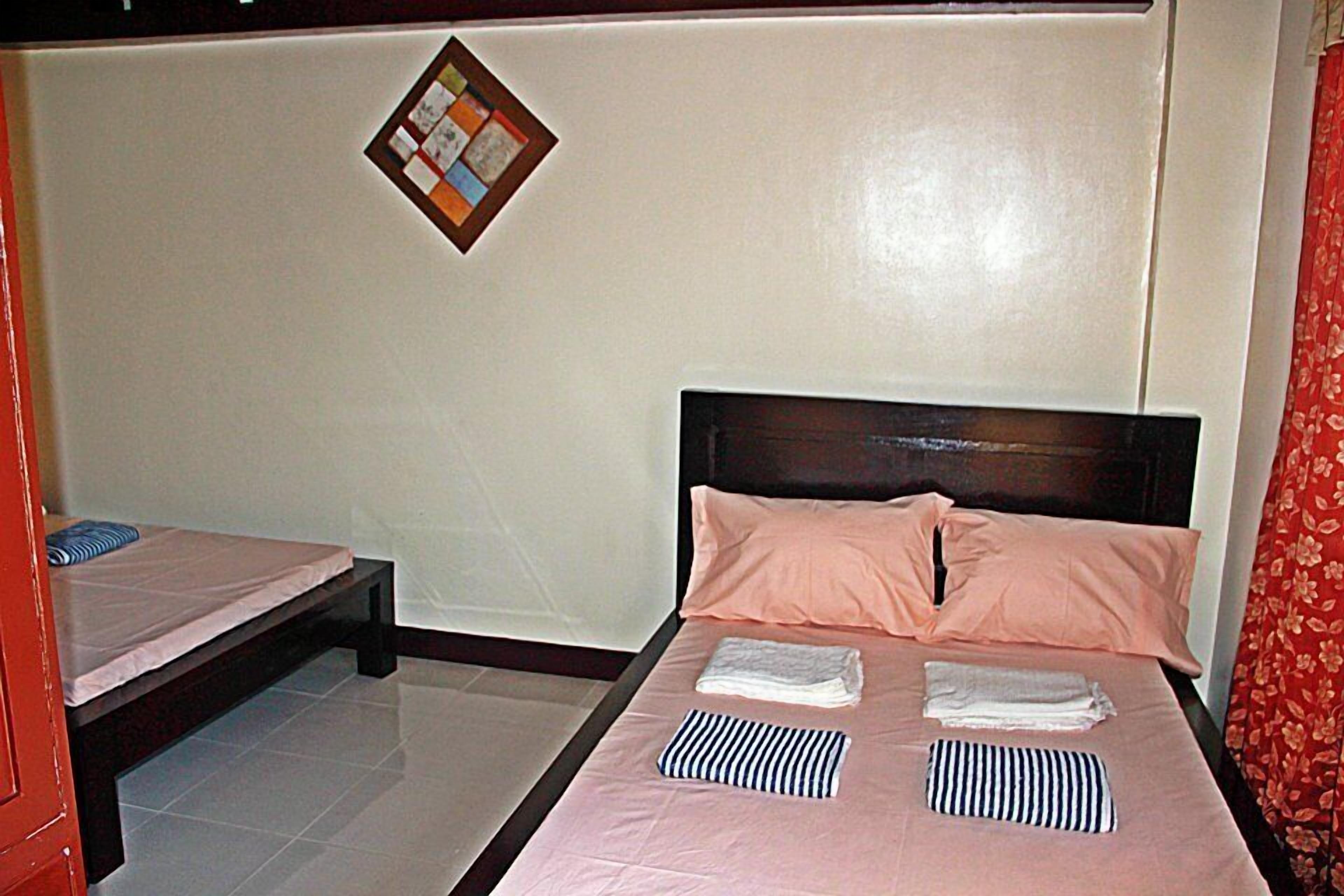 A hotel room with a single bed, a smaller bed, and a wooden headboard.