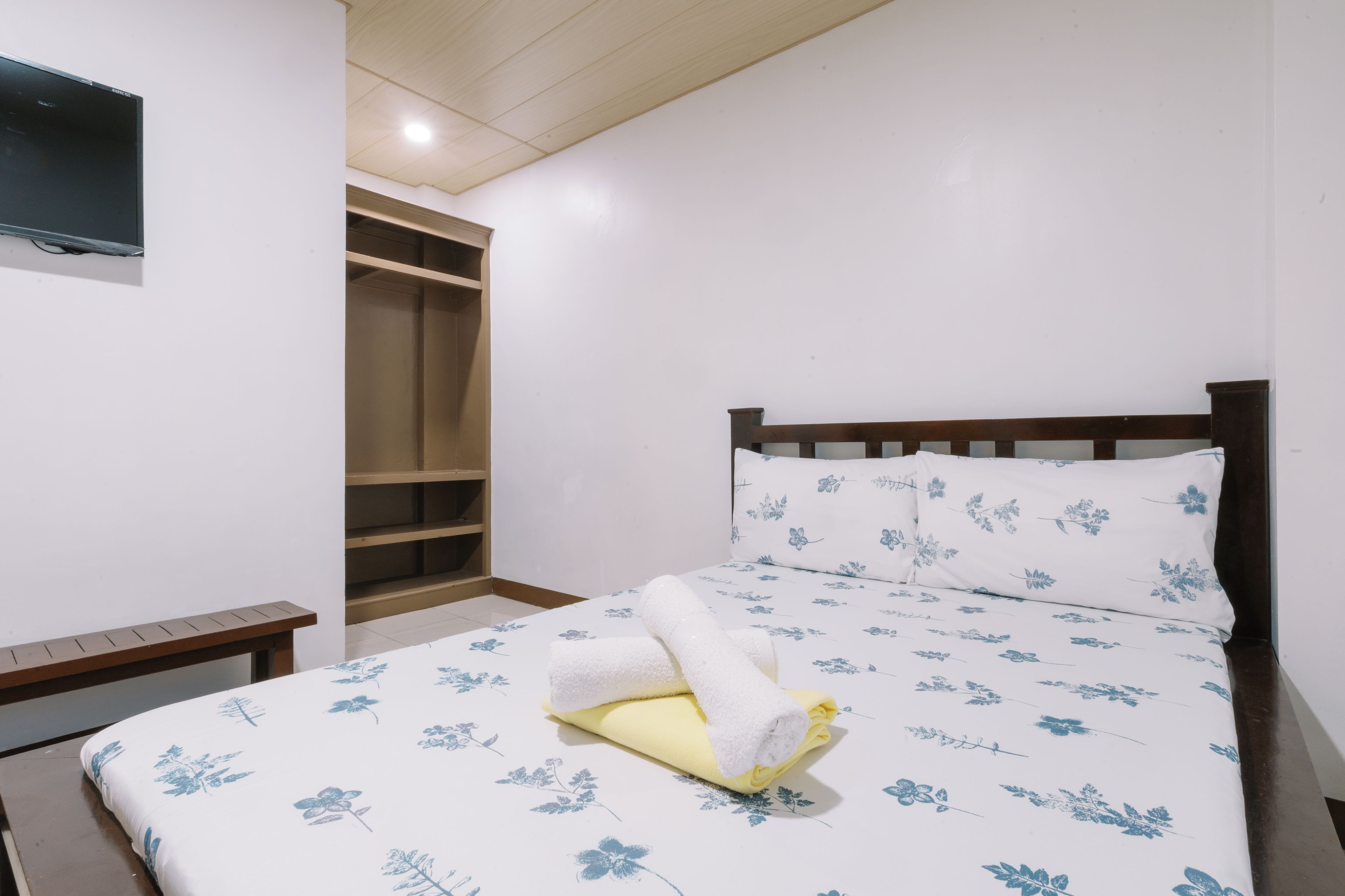 A neatly made bed with a floral bedspread, a wooden nightstand, and a built-in wardrobe with open doors.