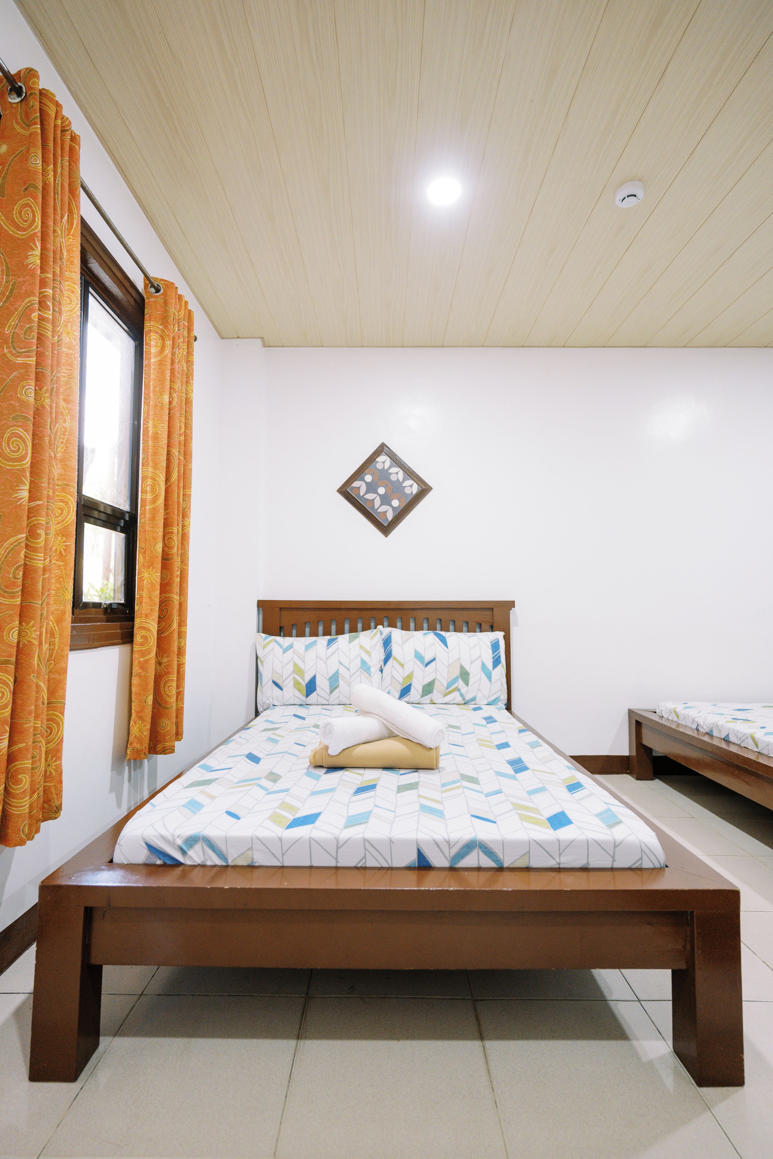 A bedroom with a wooden bed, a window with curtains, a wall-mounted light fixture, and a small decorative item.