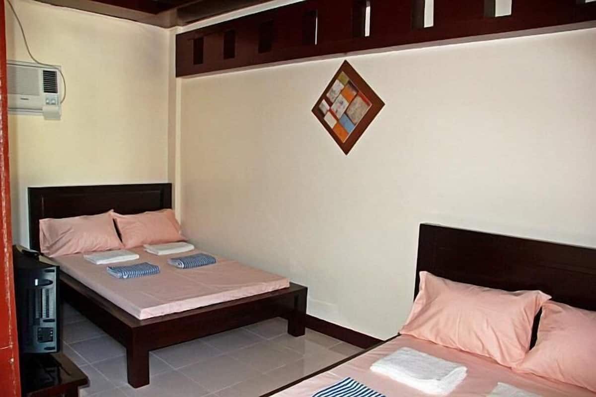 Quarto com duas camas, cabeceira de madeira, ar-condicionado fixado na parede e um quadro de avisos.