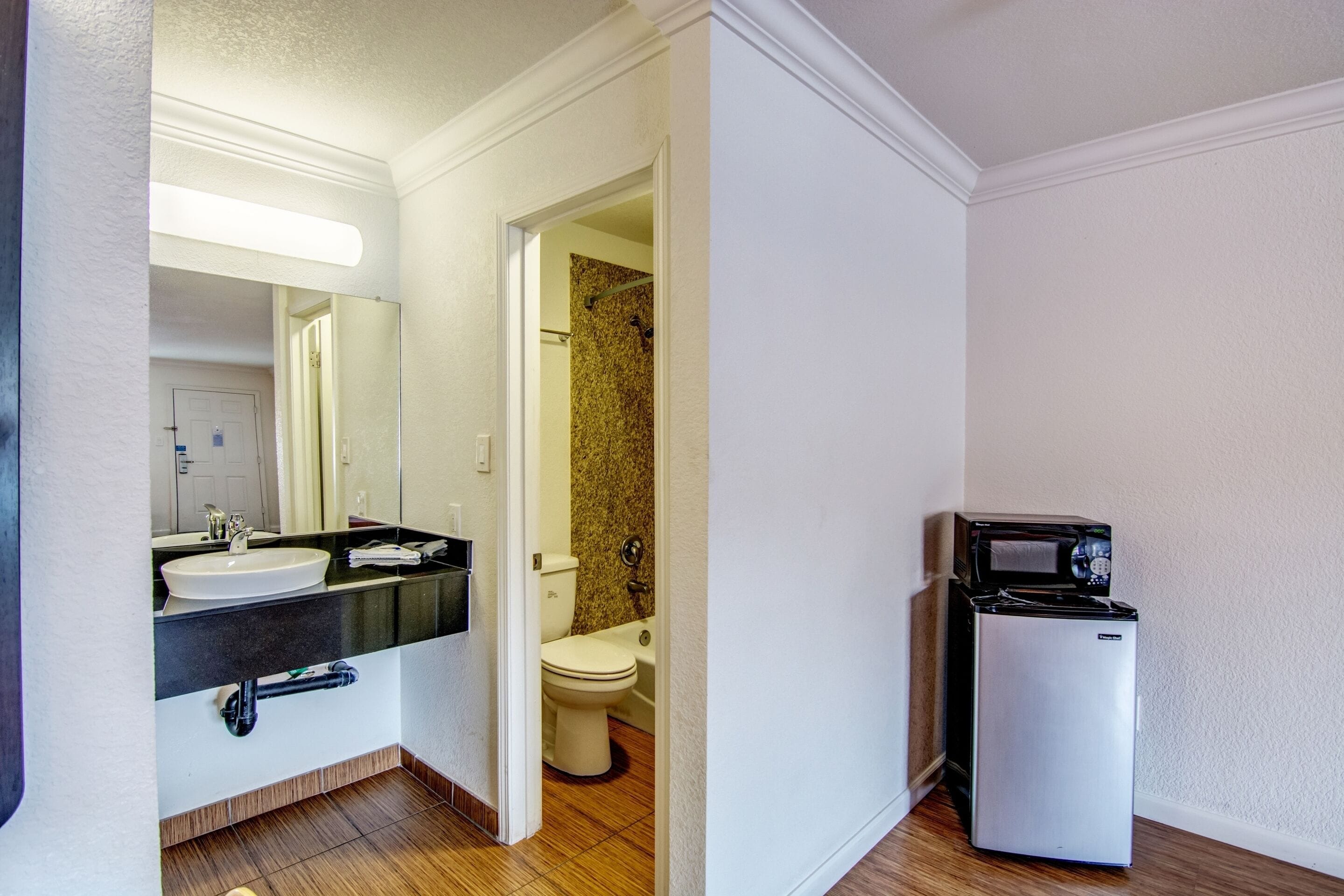 A bathroom with a sink, toilet, and a refrigerator.