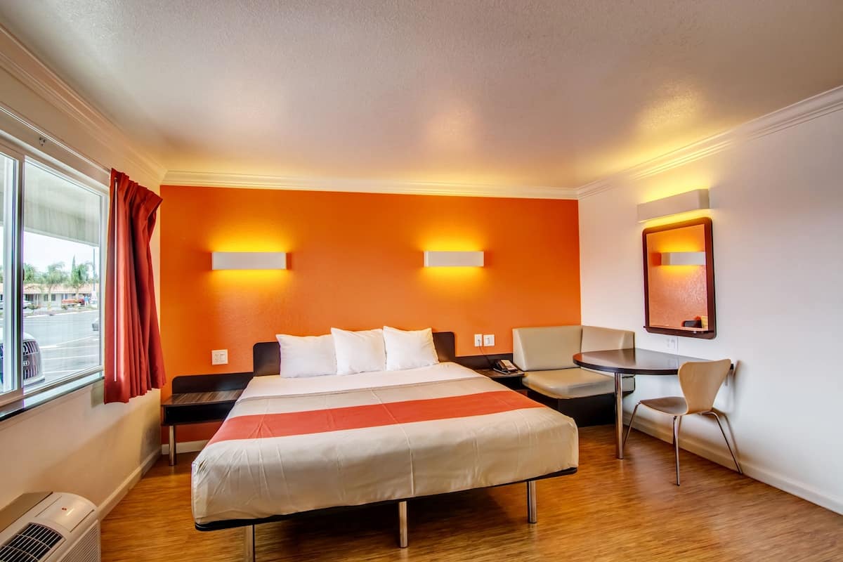 Una habitación de hotel con cama, escritorio, silla y ventana con cortinas.