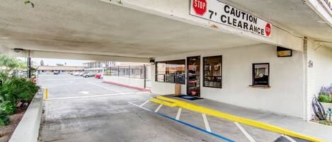 A building entrance with a stop sign and caution clearance sign, a covered parking area, and a building entrance with glass doors.