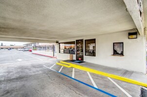 Un estacionamiento con espacios delimitados, una rampa y la entrada de un edificio con puerta y ventanas.