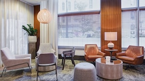A modern living room with a large window, a potted plant, and a variety of seating options including a sofa, armchairs, and ottoman. - Hyatt Place Chicago/River North (Chicago)