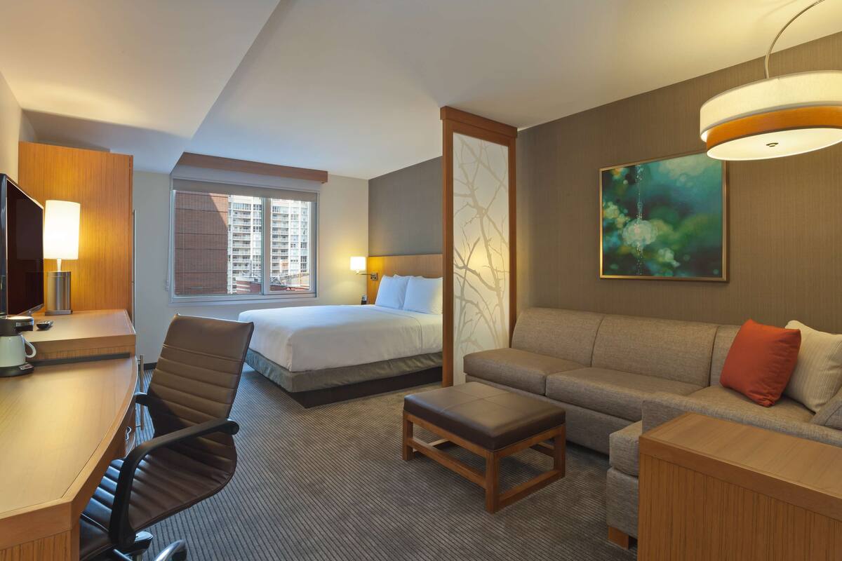 A hotel room with a bed, a sofa, a desk, and a TV.
