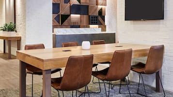 Un salón de conferencias con una larga mesa de madera, seis sillas de cuero marrón, un presentador y una televisión de pantalla plana grande montada en la pared.