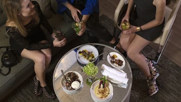 A round table with various dishes and drinks, surrounded by people seated on a couch.