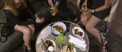 A round table with various dishes and drinks, surrounded by people seated on a couch.
