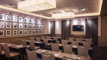 A conference room with tables and chairs, a large screen, and framed pictures on the wall.
