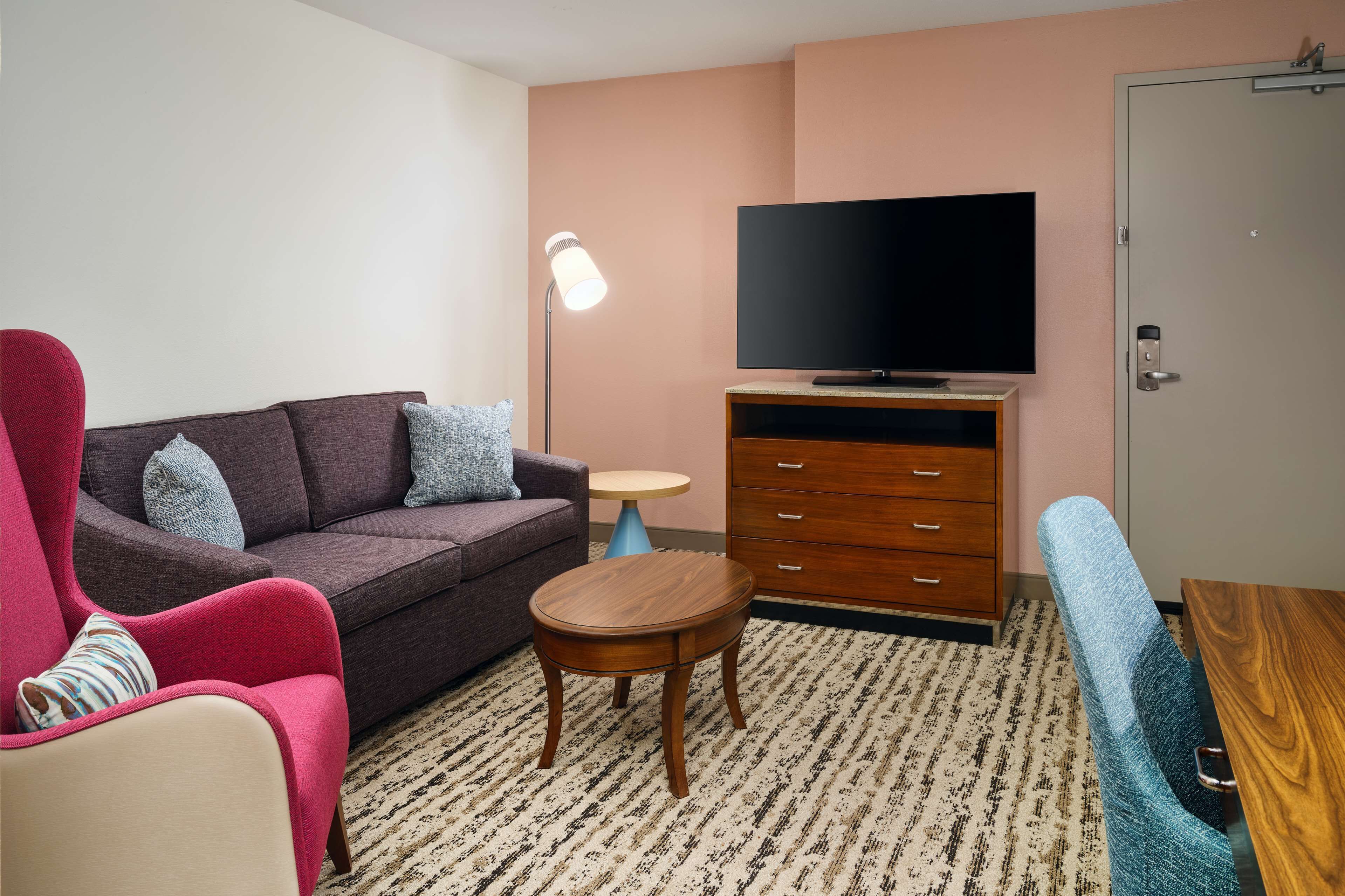 Una sala de estar con un sofá, un sillón rojo, una pequeña mesa de madera, un televisor y un aparador.