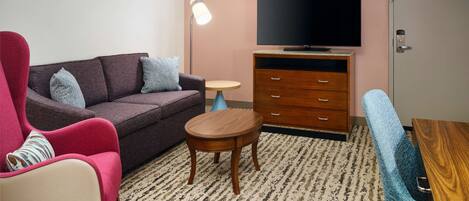 Una sala de estar con un sofá, un sillón rojo, una pequeña mesa de madera, un televisor y un aparador.