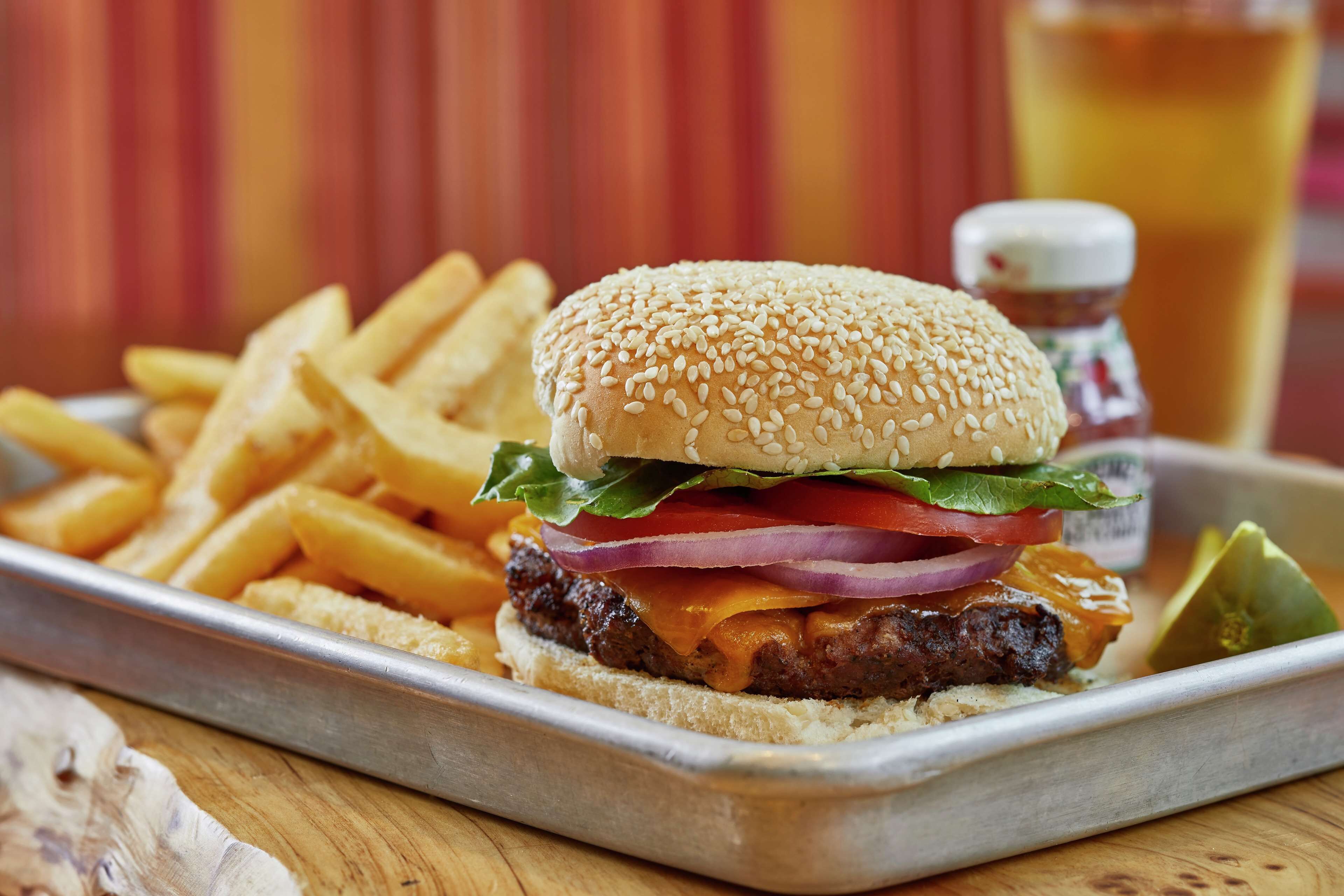 A burger with lettuce, tomato, and cheese, served with fries and a pickle on a tray.