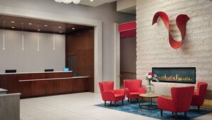 A modern hotel lobby with a reception desk, red upholstered chairs, a fireplace, and a unique wall art piece. - Hilton Garden Inn Atlanta Midtown (Atlanta)