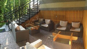 A modern outdoor lounge area with wicker furniture, a glass coffee table, and a staircase leading to an upper level. - Komilfo Hotel (Chisinau)