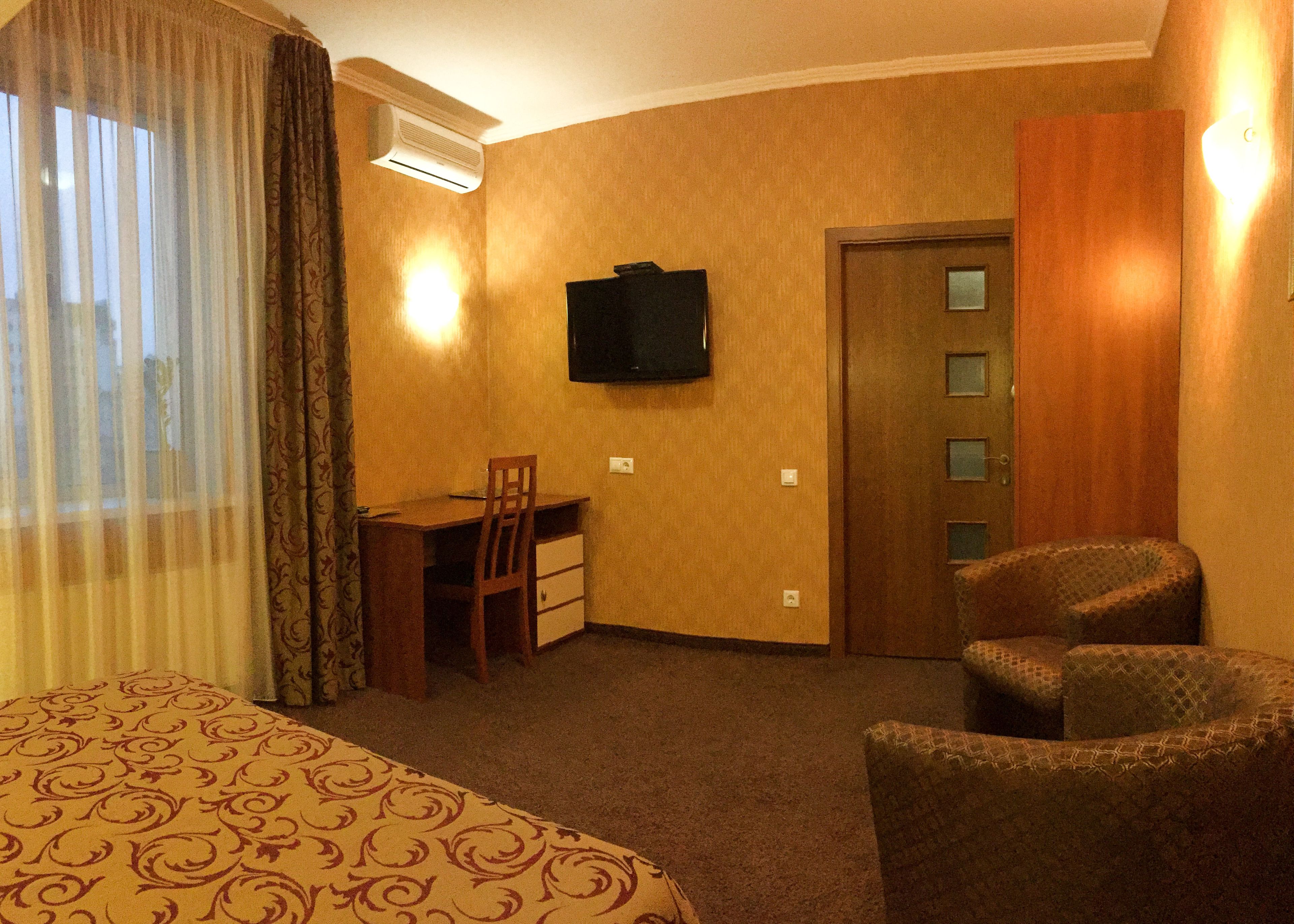 A hotel room with a bed, a desk, a chair, a television, and a door.