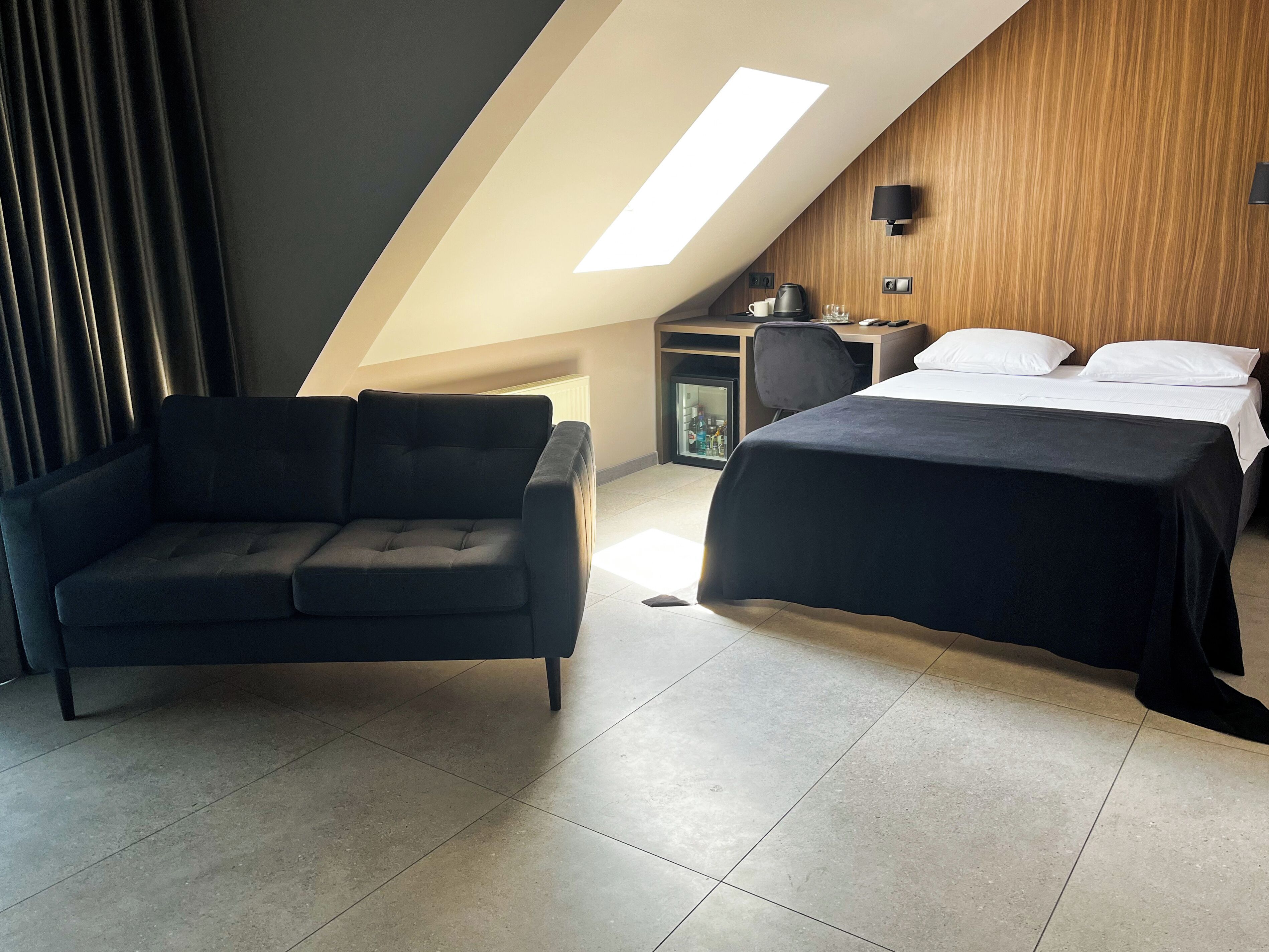 Una habitación de hotel moderna con cama tipo loft, un sofá, un escritorio y un refrigerador pequeño.