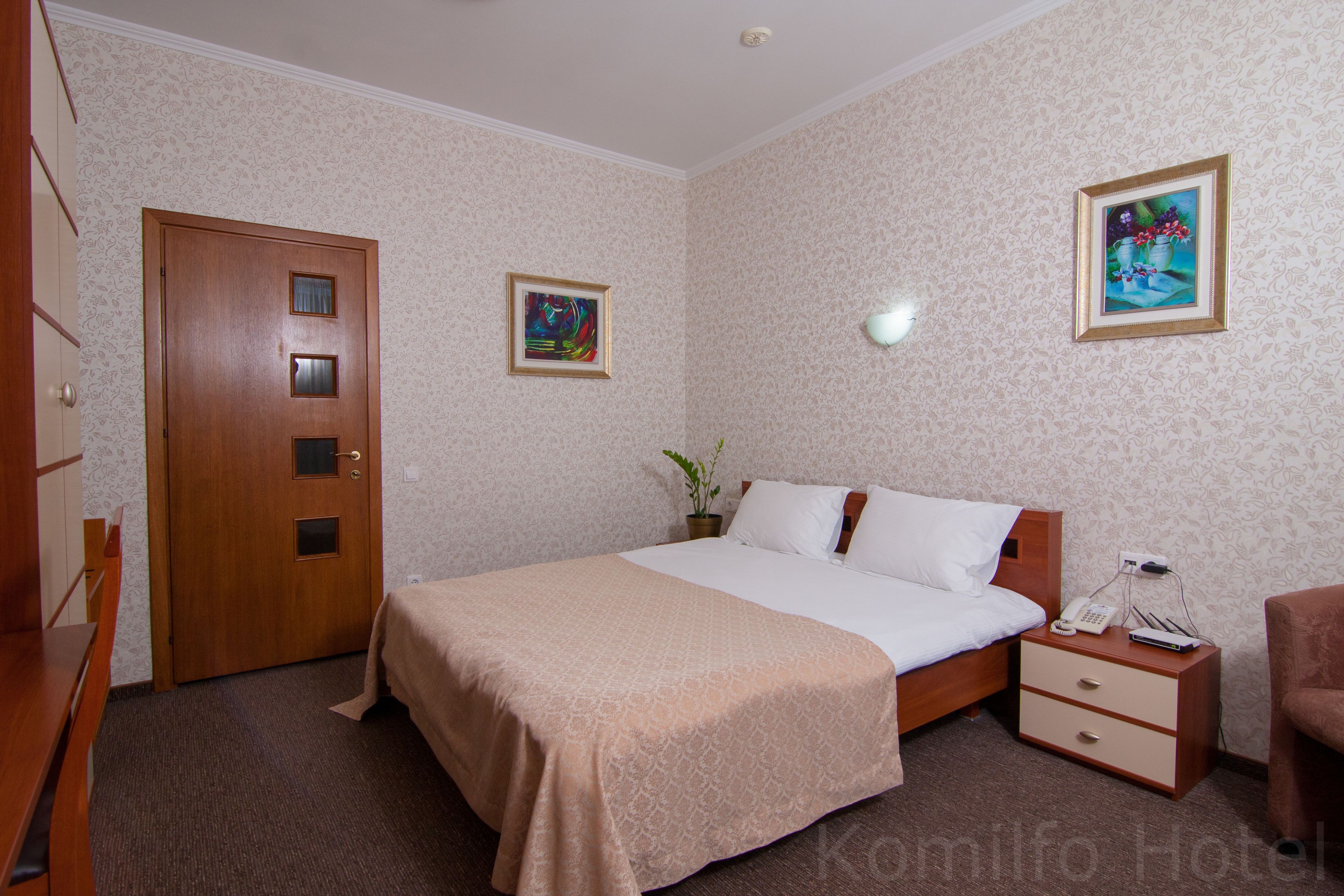 A hotel room with a bed, bedside table, lamp, and a door.
