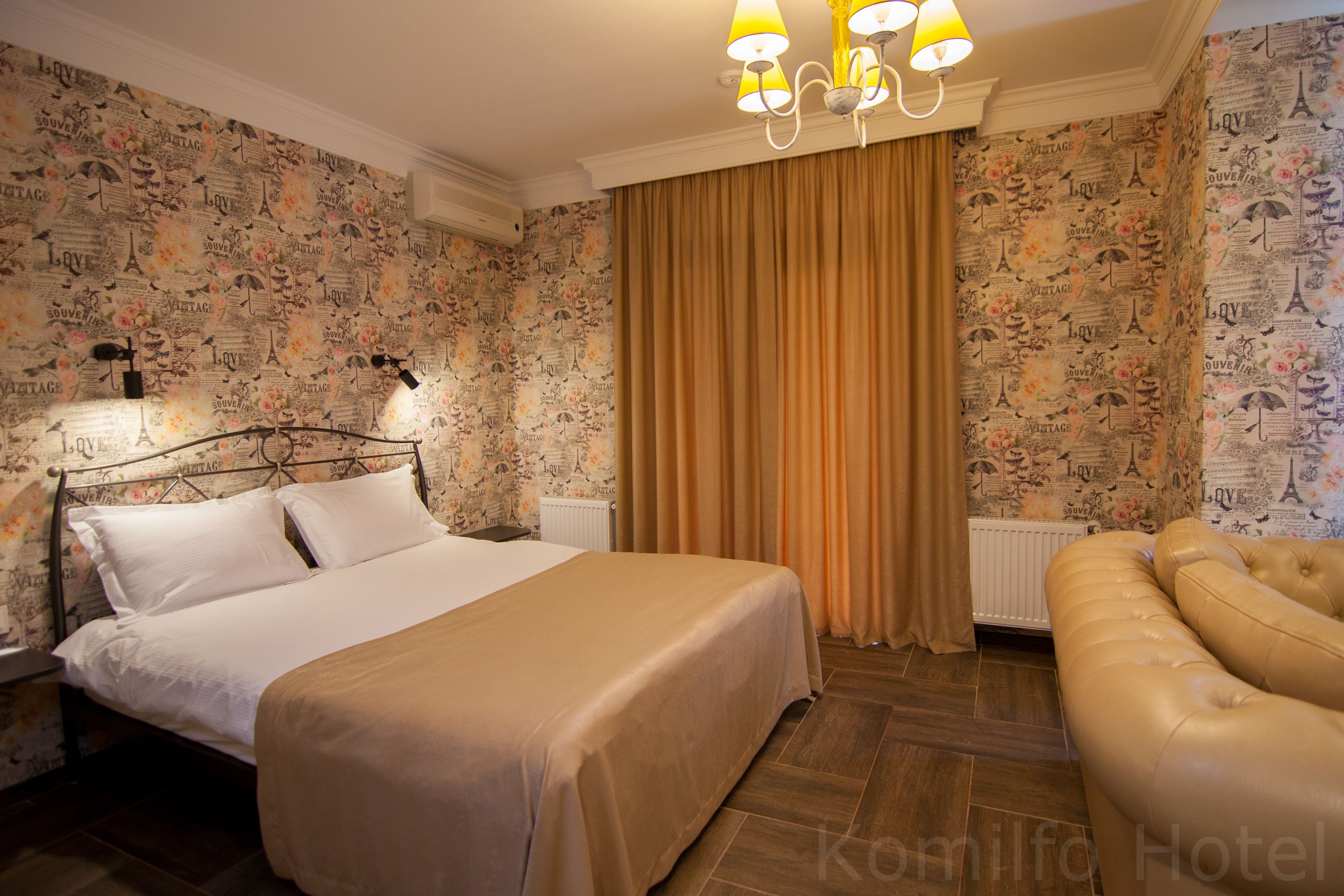 Una habitación de hotel con cama, sofá, candelabro y papel tapiz con texto e ilustraciones de estilo vintage.