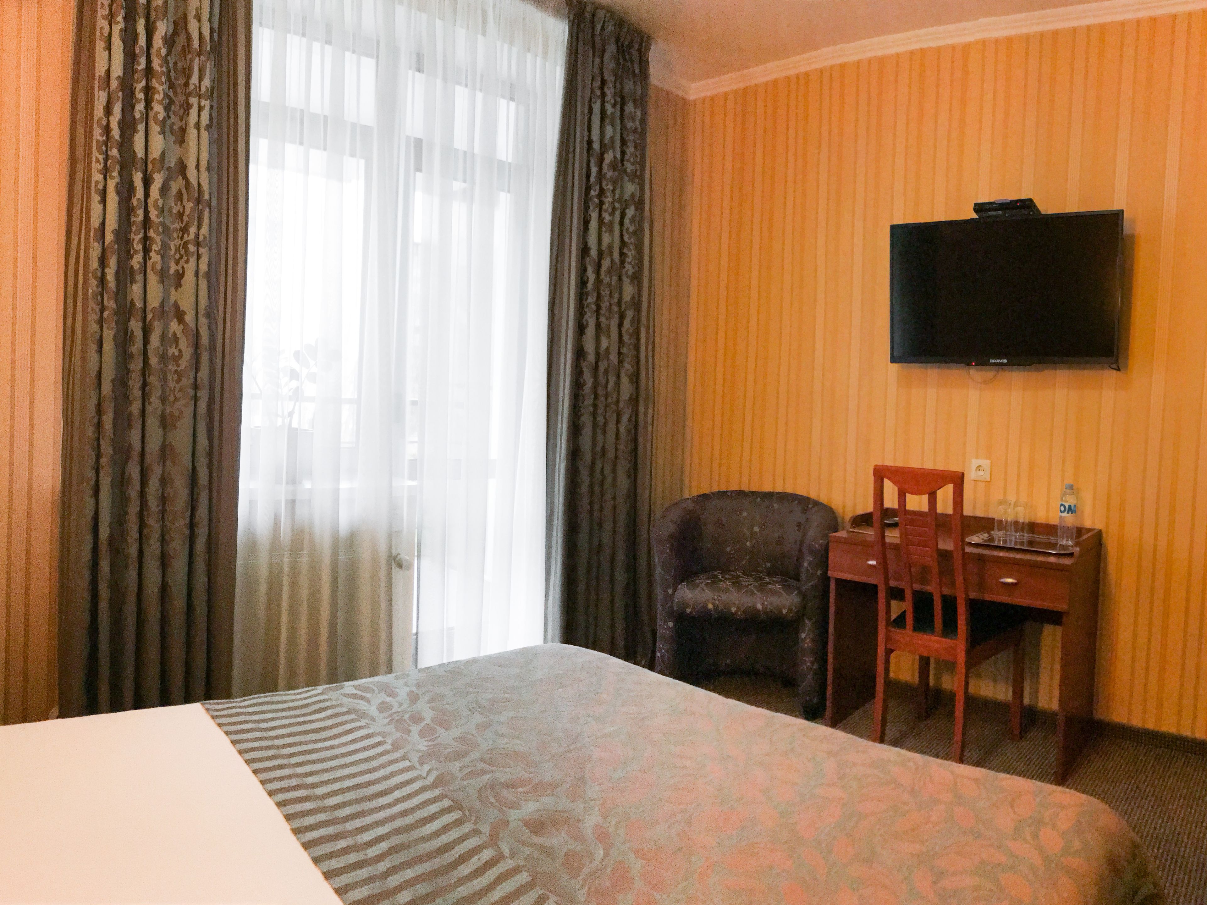 Habitación de hotel con cama, escritorio, silla, televisor montado en la pared y ventana con cortinas.