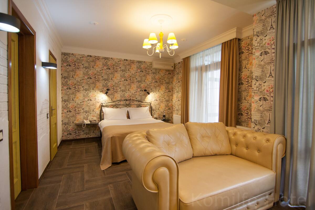 Habitación de hotel con cama, sofá, candelabro y papel tapiz con motivos florales.