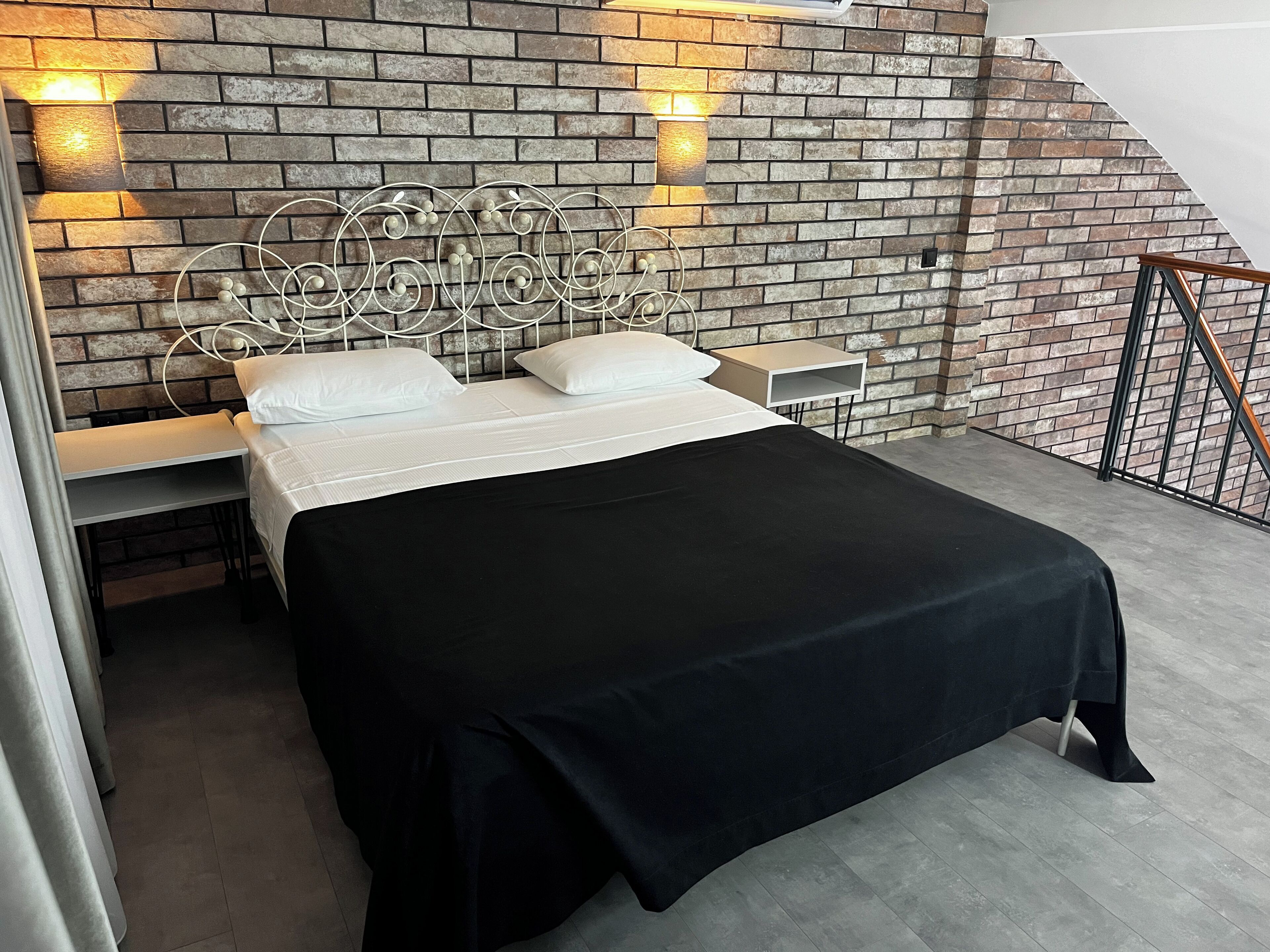 A bedroom with a brick-patterned wall, a metal headboard, a black bedspread, and bedside tables with lamps.