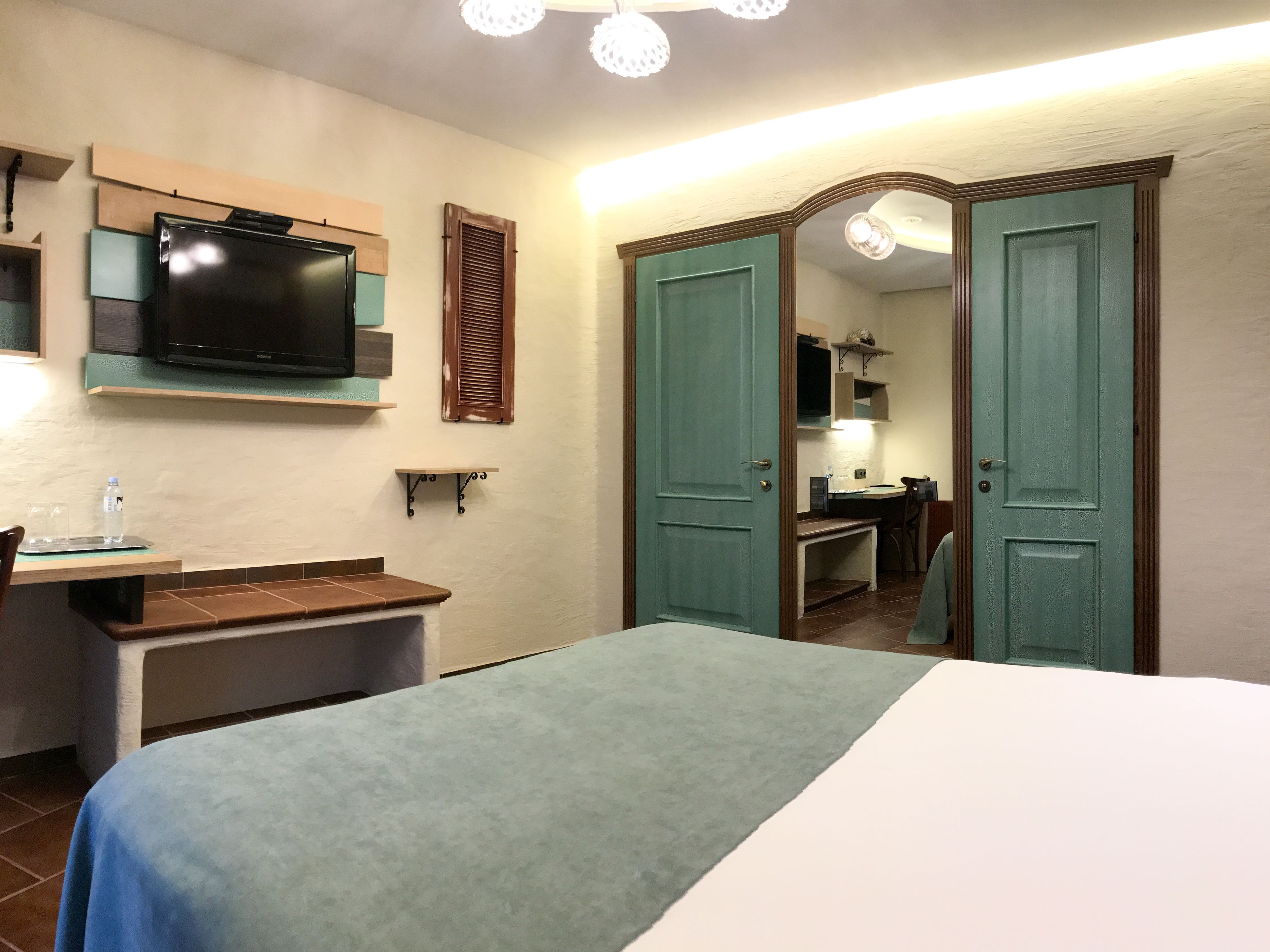 Habitación de hotel con cama, escritorio con silla, televisión y baño visible a través de una puerta abierta.