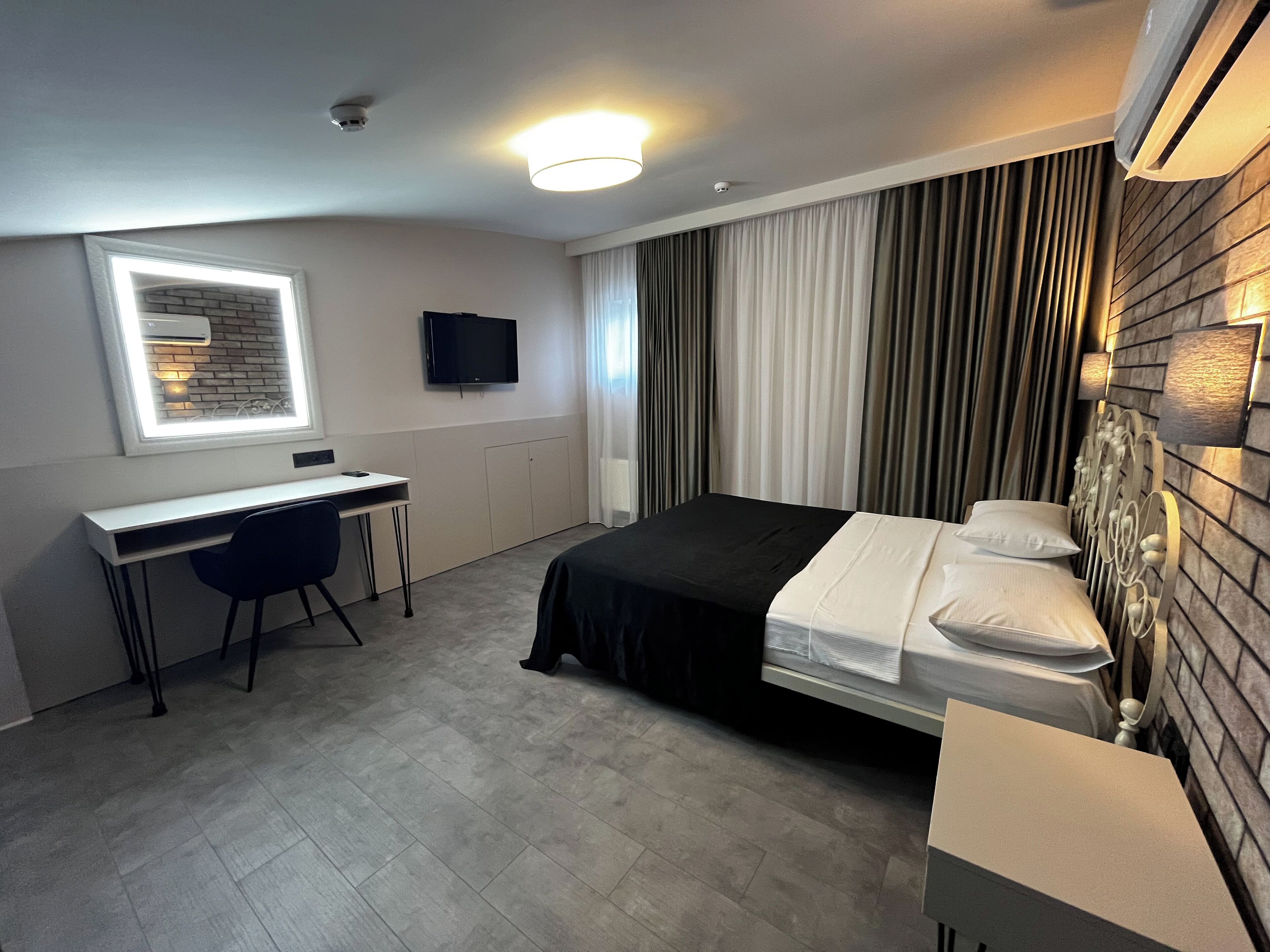 A modern hotel room with a bed, a desk, a chair, a television, and a window with curtains.