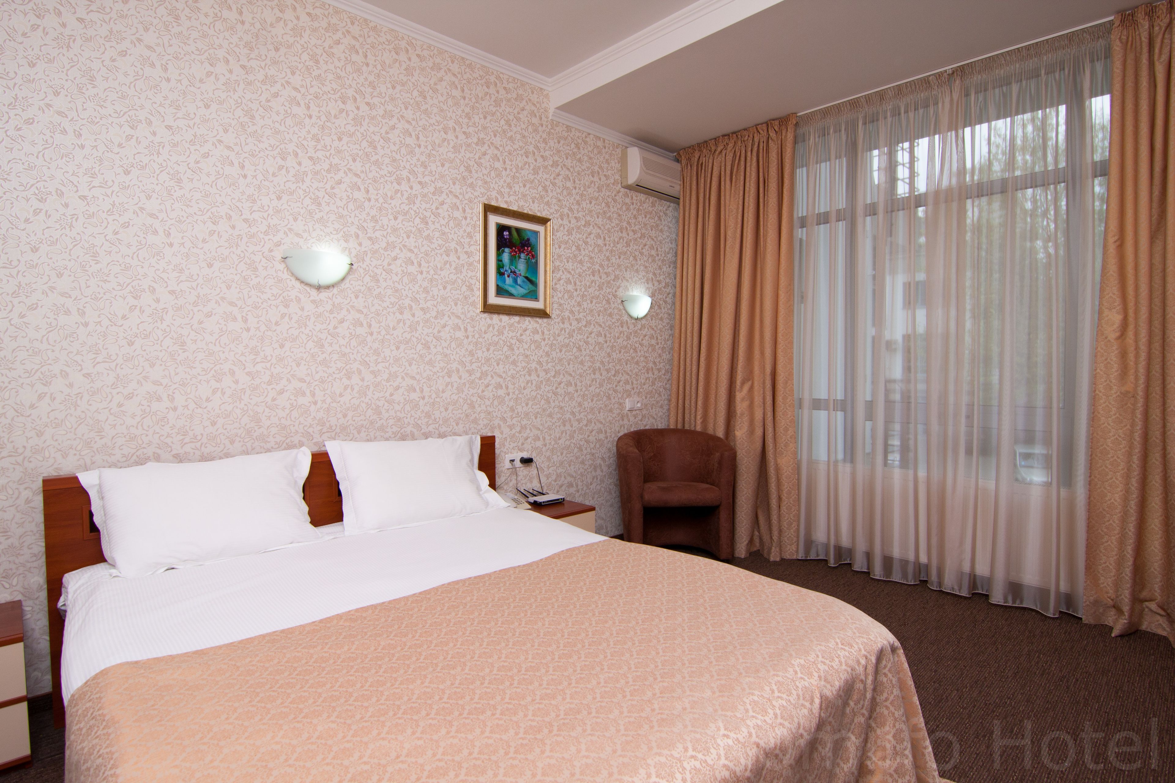 A hotel room with a large bed, a chair, a nightstand, and a painting on the wall.