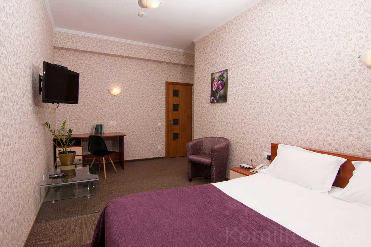 Una habitación de hotel con cama, escritorio, silla, televisor y puerta.