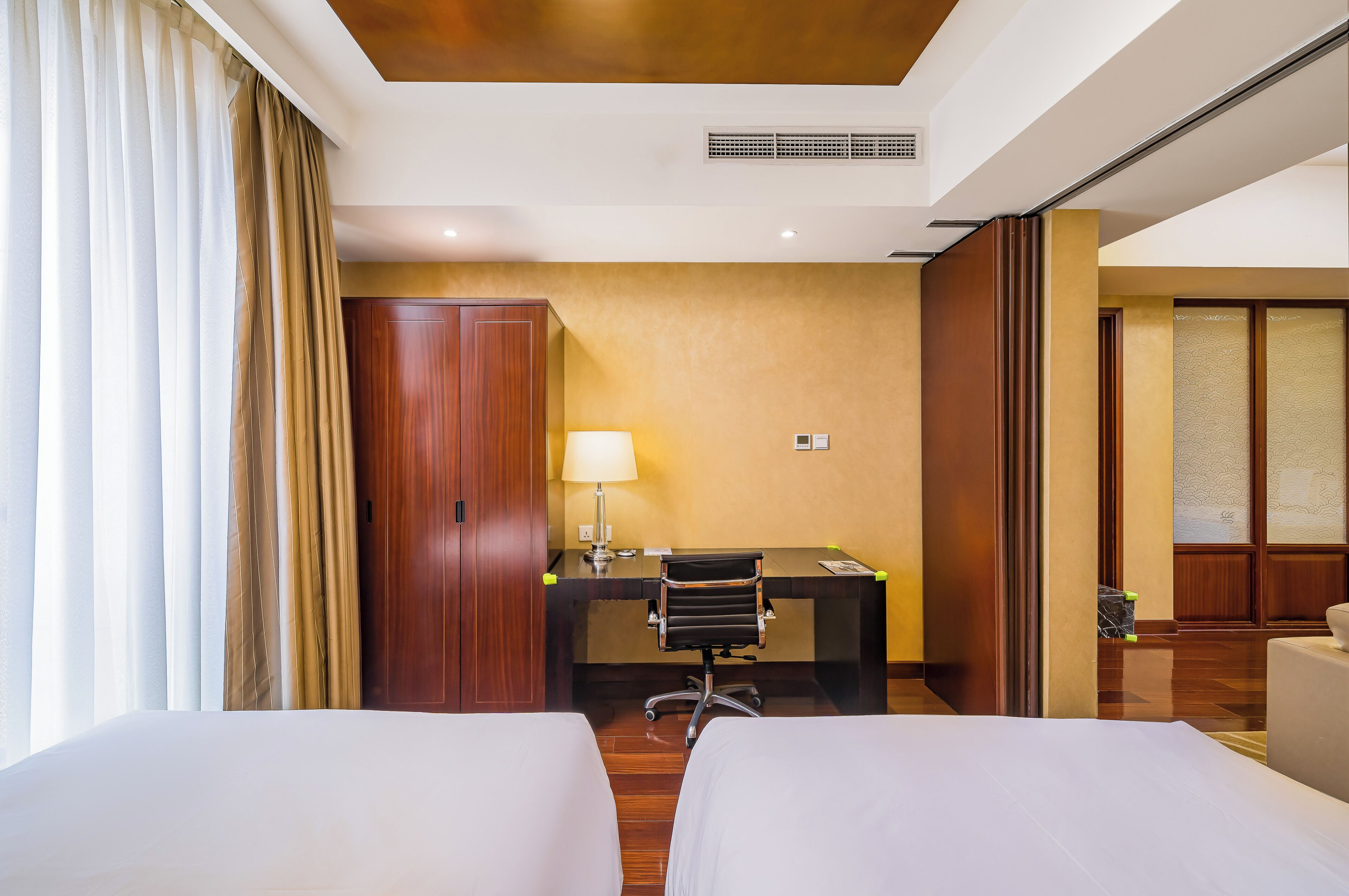 A hotel room with two beds, a desk, a chair, a lamp, and a wardrobe.