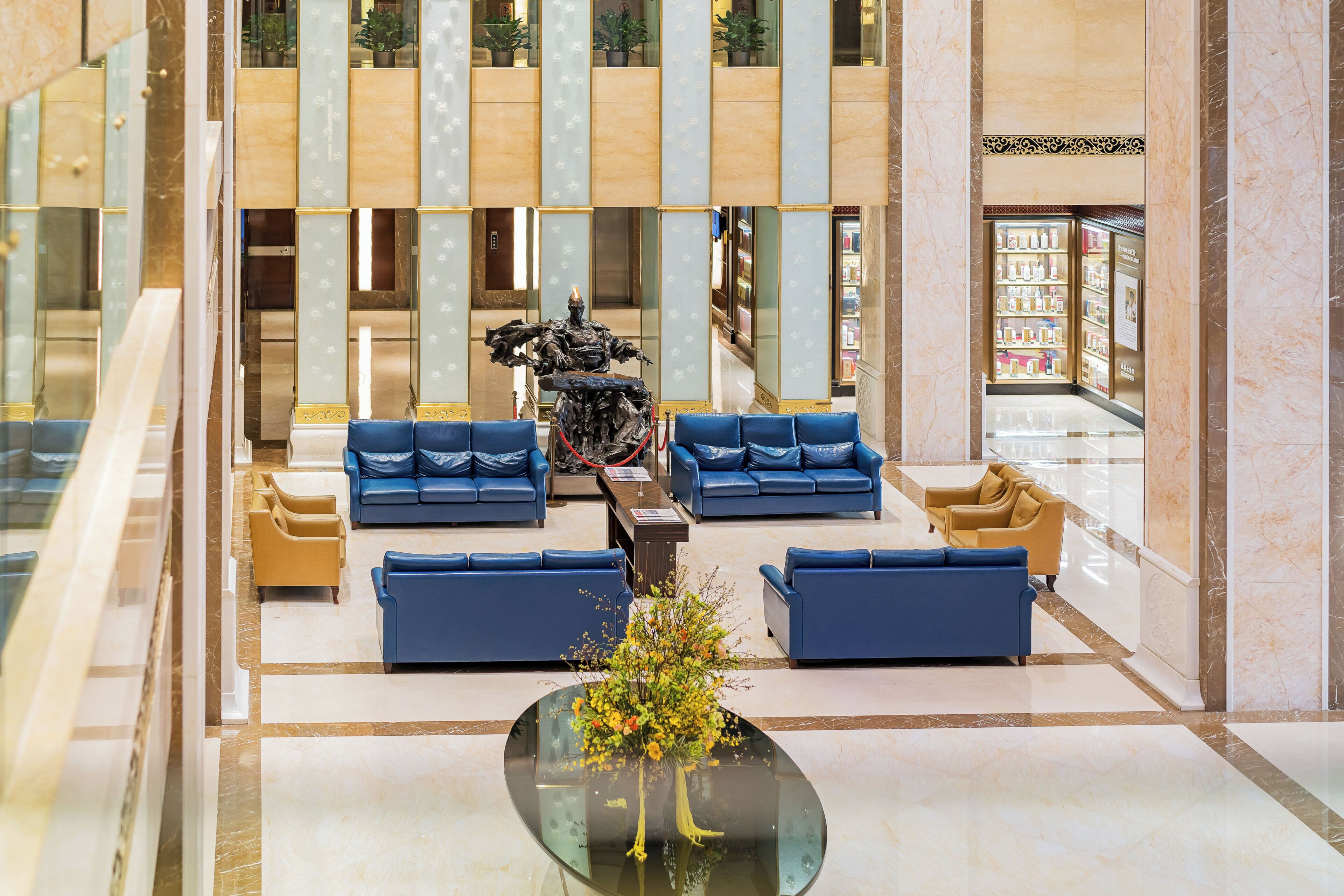 Un hall d’entrée avec des canapés bleus, une table basse en verre agrémentée d’un arrangement floral et une statue au centre.
