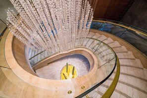 A spiral staircase with a central yellow circular platform, marble steps, and hanging crystal decorations.