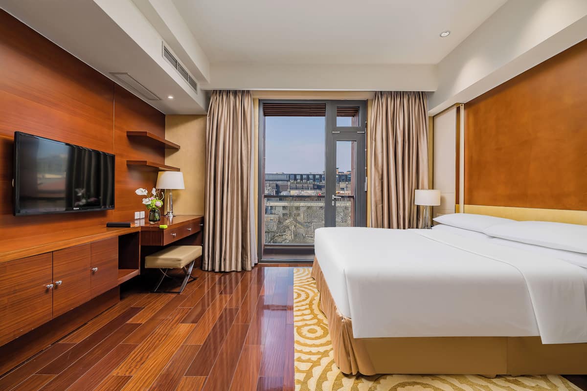 A hotel room with a bed, TV, desk, and a view of the city.