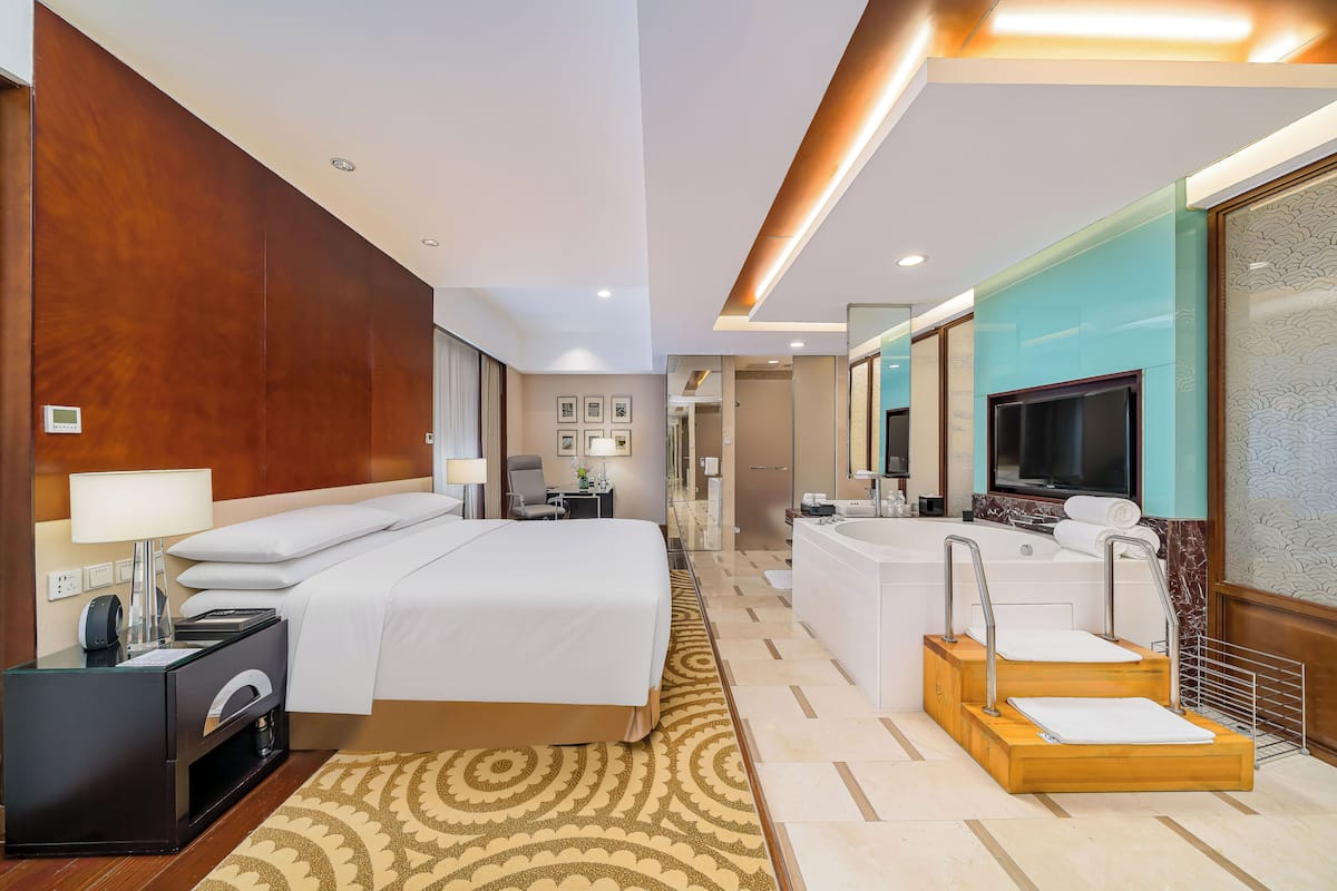 A hotel room with a bed, bedside table, lamp, TV, and a bathroom with a bathtub and shower.