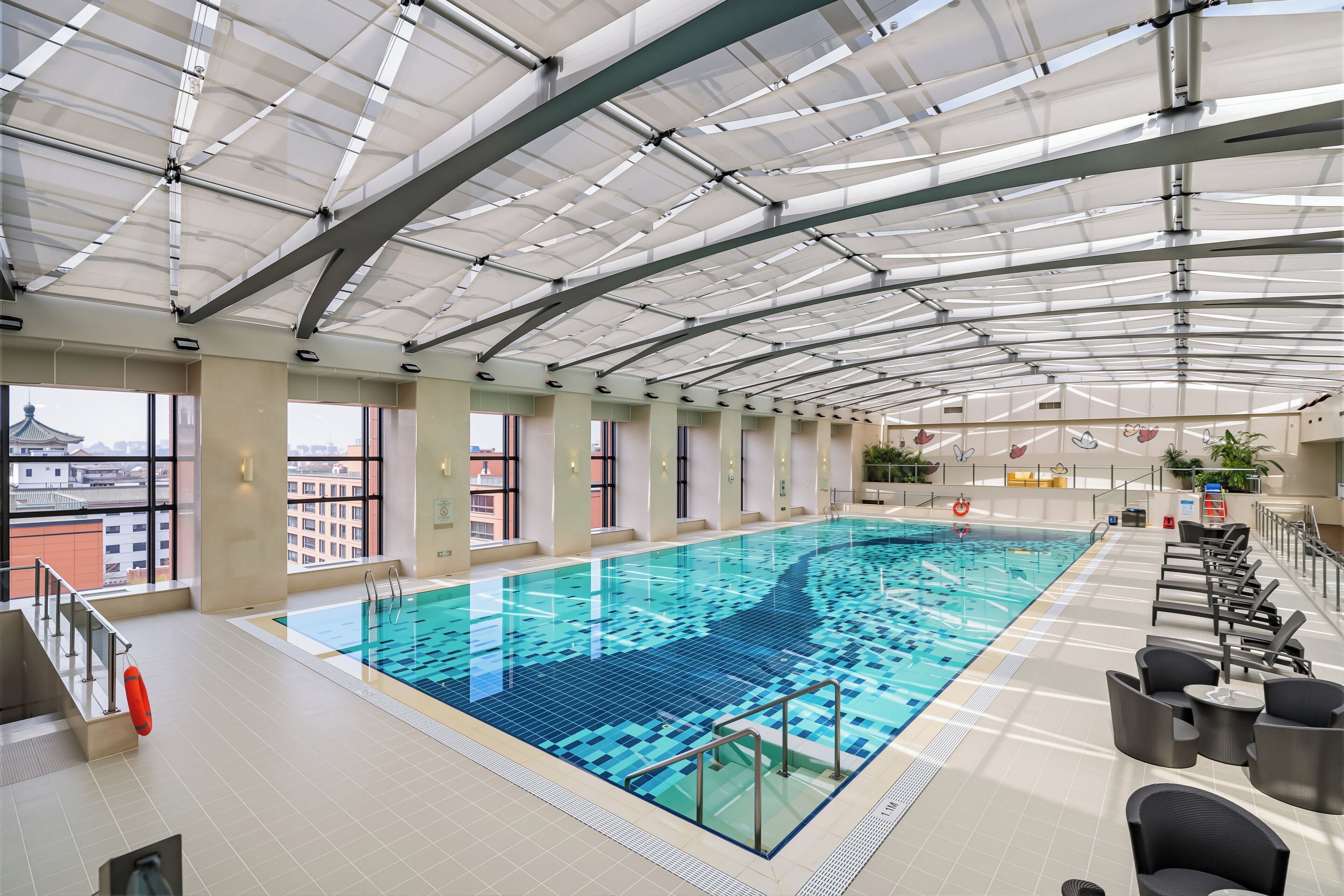 An indoor swimming pool with clear glass ceilings, a lifeguard chair, and a poolside seating area.
